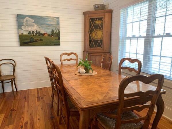 Een eetkamer met een houten tafel, zes stoelen en een schilderij aan de muur.
