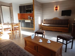 Um espaço compacto com cozinha compacta, um sofá, uma mesa de jantar e uma TV fixada na parede.
