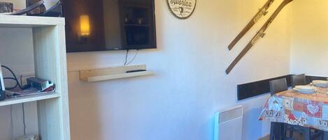 Un comedor con una mesa dispuesta para dos personas, un televisor montado en la pared y esquíes apoyados en la pared.