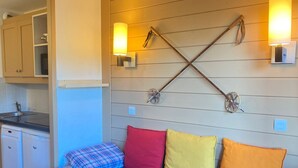 A compact room with a bed, a kitchenette, and a wall-mounted light fixture.