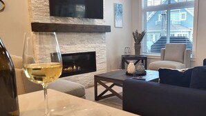 A living room with a fireplace, a sofa, a coffee table, and a glass of wine.
