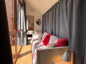 Un dormitorio con cama, lámpara de noche, espejo y ventana con cortinas.