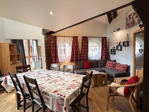 A cozy living area with a dining table, chairs, a sofa, and a bookshelf.
