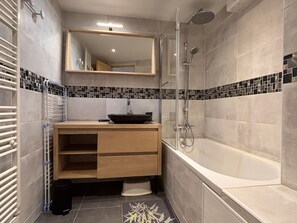 A bathroom with a bathtub, a sink with a vessel basin, a mirror, and a shower.
