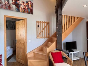 A staircase with wooden railings, a television on a white stand, and a wicker chair with a red cushion.