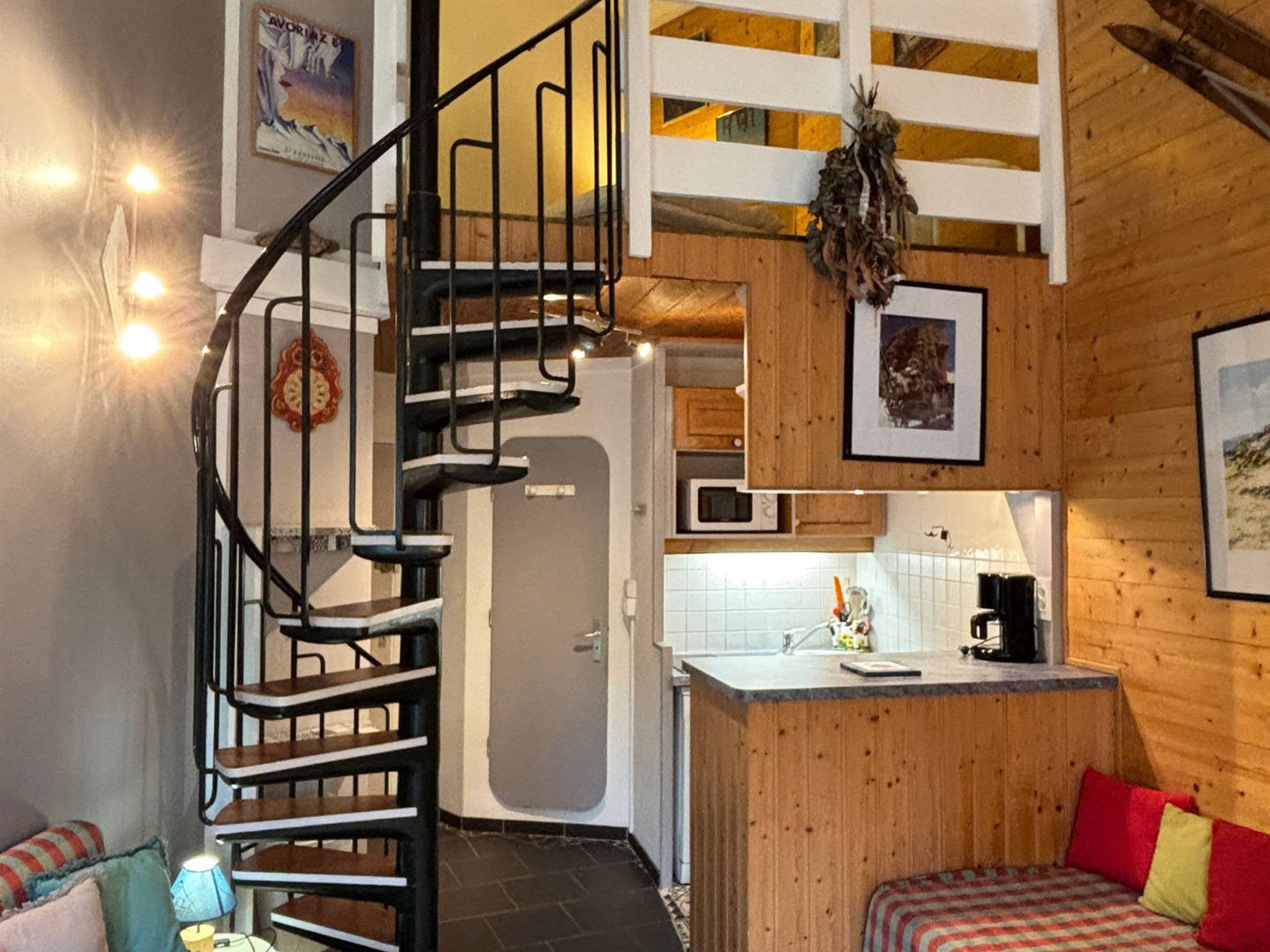 Une cuisine compacte dotée d’un four à micro-ondes encastré, d’un petit îlot central et d’un escalier en colimaçon menant à un niveau supérieur.