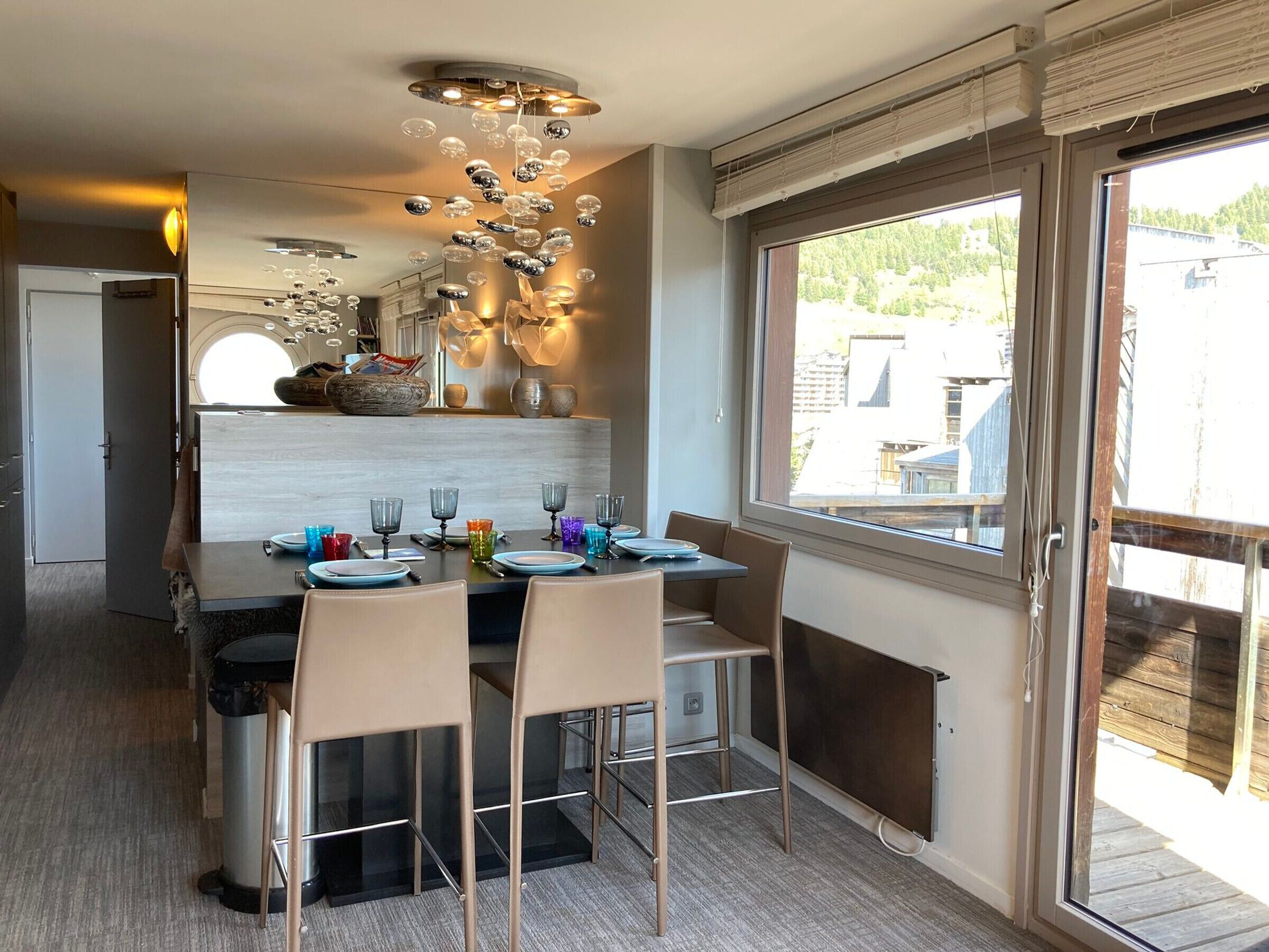 Un comedor moderno con una mesa central dispuesta para cuatro personas, rodeada de sillas. Una lámpara de techo original con elementos esféricos cuelga encima.