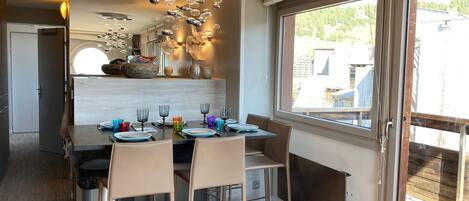 Un comedor moderno con una mesa central dispuesta para cuatro personas, rodeada de sillas. Una lámpara de techo original con elementos esféricos cuelga encima.