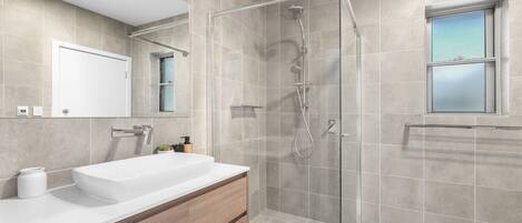 A modern bathroom with a glass-enclosed shower, a white sink, and a mirror above it.