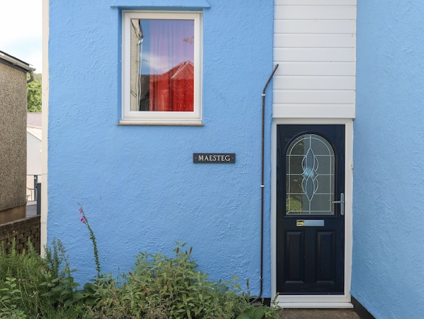 Una casa azul con una puerta negra y una ventana con cortina roja.
