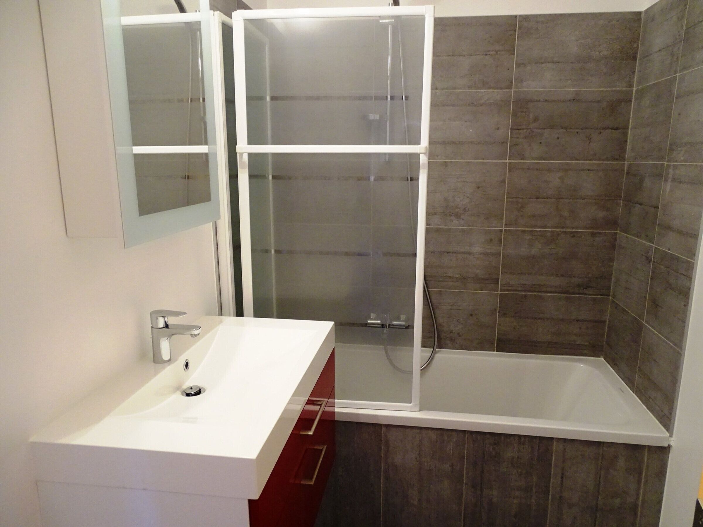 A bathroom with a white sink, a glass shower enclosure, and dark wooden tiles.