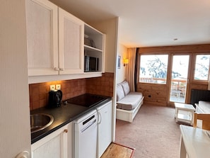 A compact kitchen with a microwave, a sink, and a dishwasher. There is a seating area with a sofa and a table, and a window with a view of a snowy landscape.