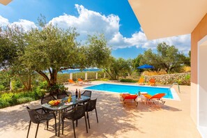 A pool area with a table and chairs, surrounded by trees and a clear sky. - Villa Eri in Vlachata (Kefalonia)