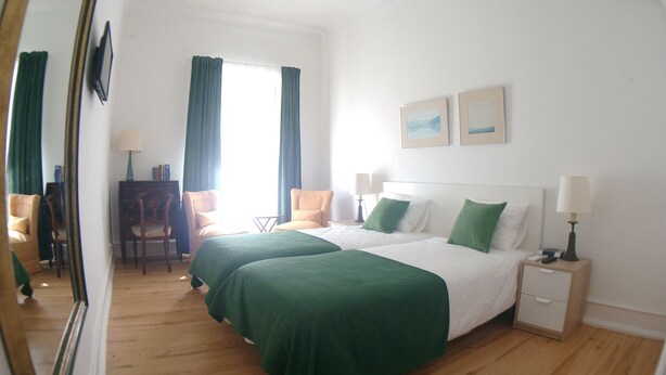 A hotel room with two beds, a desk, a chair, and a window with curtains. - Comfort and quiet in Lisbon center (Lisboa)