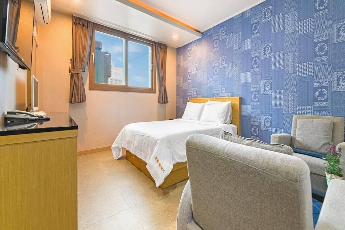 Ein Hotelzimmer mit einem Bett, einem Schreibtisch mit Telefon, einem Sessel und einem Fenster mit Vorhängen.