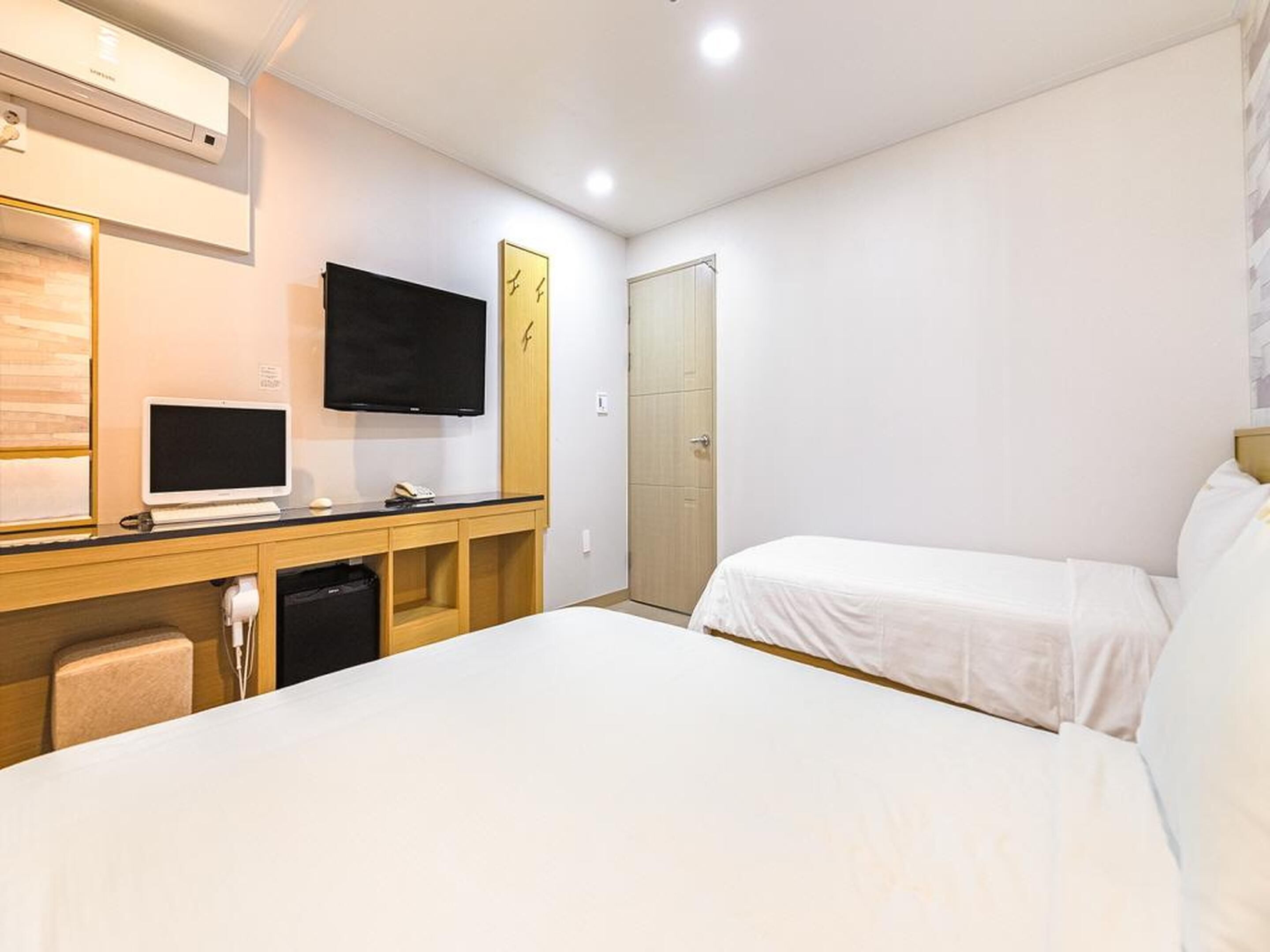 A hotel room with two beds, a desk with a computer and phone, a TV, and a wardrobe.