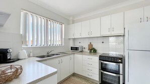 A modern kitchen with white cabinets, a microwave, a stove, and a sink. - Tuncurry Treasure, Central Location (Tuncurry)