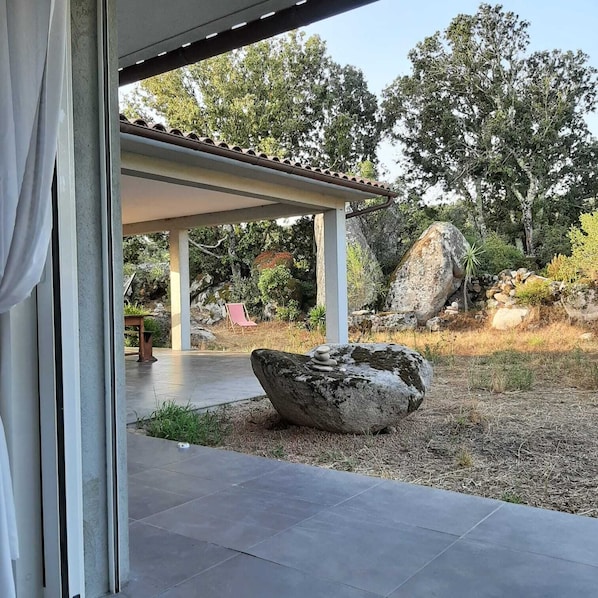 A covered outdoor area with a stone structure, a large rock, and a red chair. - Spacious villa in a quiet location between Porto Vecchio and Figari (Sotta)
