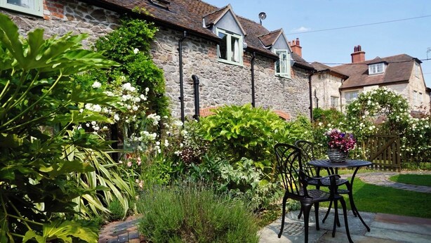 A stone house with a garden patio, a table with chairs, and a variety of plants and flowers.