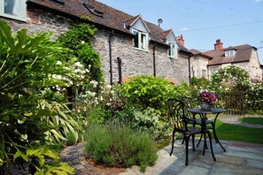 A stone house with a garden patio, a table with chairs, and a variety of plants and flowers. - Nest Holiday Hideaway Dove Barn Amazing Location! (Church Stretton)