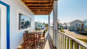 A wooden deck with a table and chairs, overlooking a residential area with houses. - 3 Story Home with Elevator, Walk to Beach, Shared Pool and Golf Cart Included (Port Aransas)