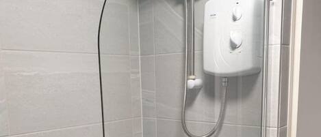 Cabina de ducha con paredes de vidrio, cabezal de ducha de mano y panel de control en la pared.
