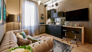 A modern living room with a sofa, a coffee table, and a TV. There is a kitchen area with a counter and stools. - My Home For You - Tasso (Bergamo)