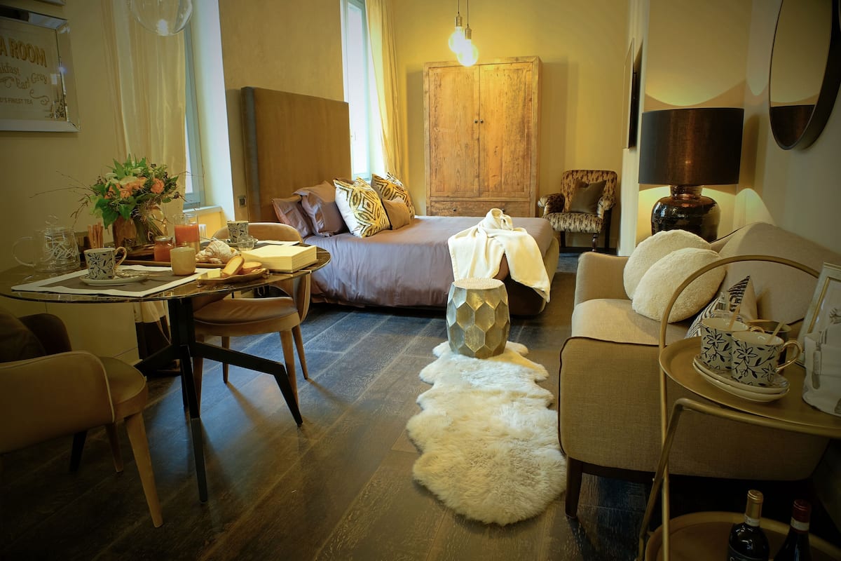 Una habitació d'hotel acollidora amb un llit, zona de menjador, sofà i taula petita amb làmpada.