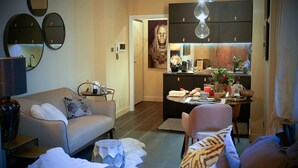 A modern living room with a sofa, a dining area with a table set for two, and a kitchen with dark cabinets and pendant lighting. - My Home For You - Tasso (Bergamo)