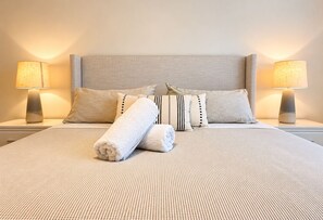 Un lit bien fait, avec une couvre-lit à rayures, deux oreillers et deux lampes de chevet.