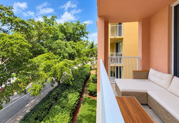A balcony with a white sofa and a wooden table, overlooking a road with trees and a clear sky. - LUXURY THE YATCH 402- FREE PARKING AND WIFI (Aventura)