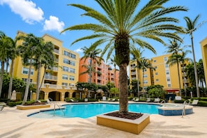 Un resort con piscina central, palmeras y edificios de varios pisos con balcones.