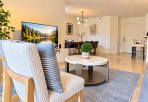 Un salon moderne avec un canapé, une table à manger et un téléviseur diffusant un paysage pittoresque.