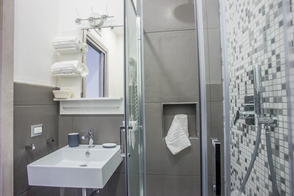 A modern bathroom with a glass-enclosed shower, a sink with a mirror above it, and a tiled wall. - Solarium al Duomo - Suite 1 by Wonderful Italy (Napoli)