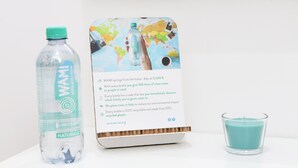Une bouteille d’eau de la marque WAMI, une brochure et une bougie de couleur turquoise, le tout posé sur une surface blanche.