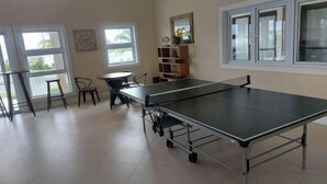 A room with a ping pong table, chairs, a small round table, and a bookshelf. - Beautiful home and secure Community. (Lucea)