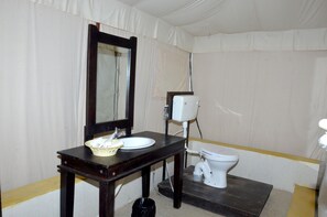 A bathroom with a wooden vanity, a white sink, a mirror, a toilet, and a white toilet paper holder.