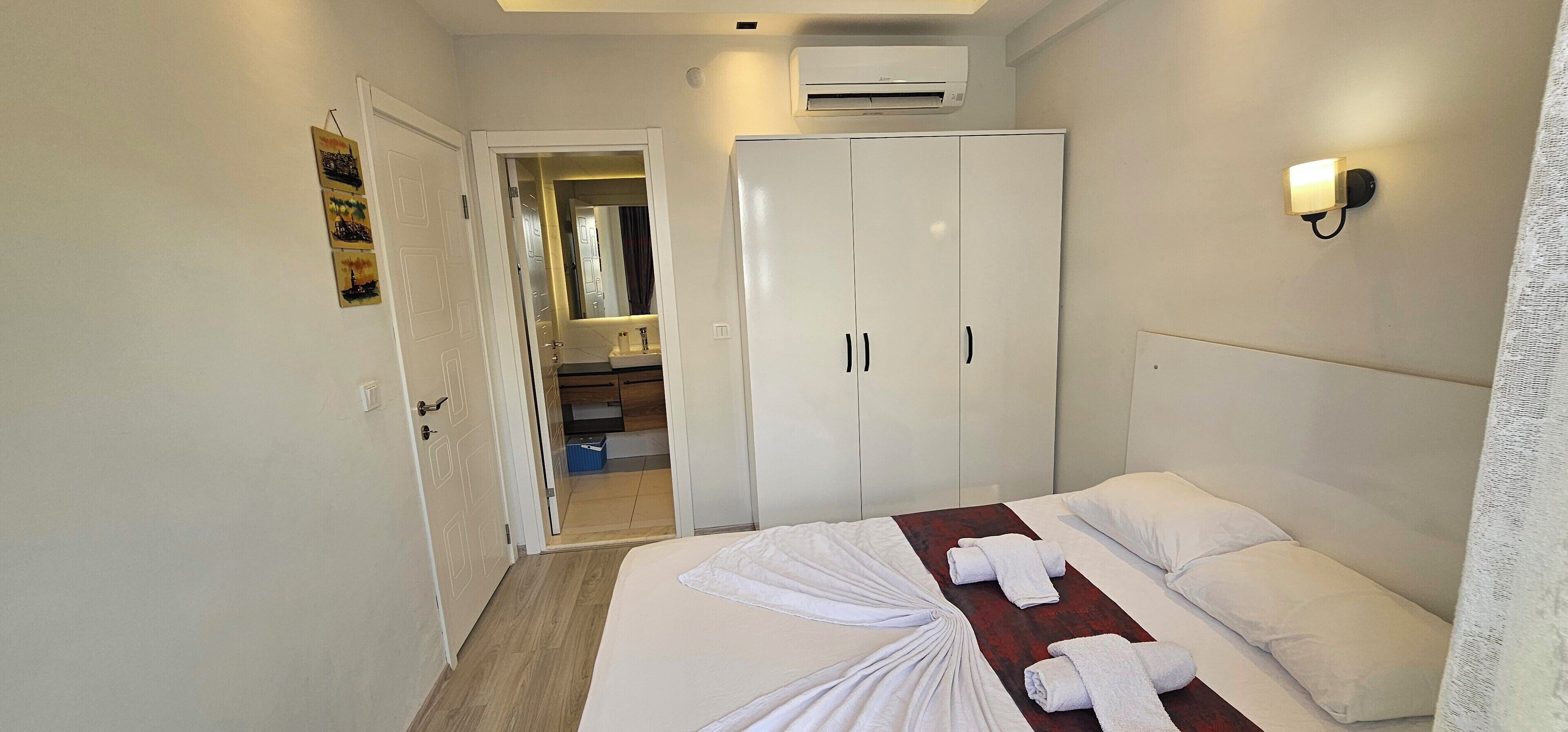 Une chambre d’hôtel équipée d’un lit, d’une armoire, d’un appareil de climatisation et d’une salle de bain visible à travers une porte ouverte.