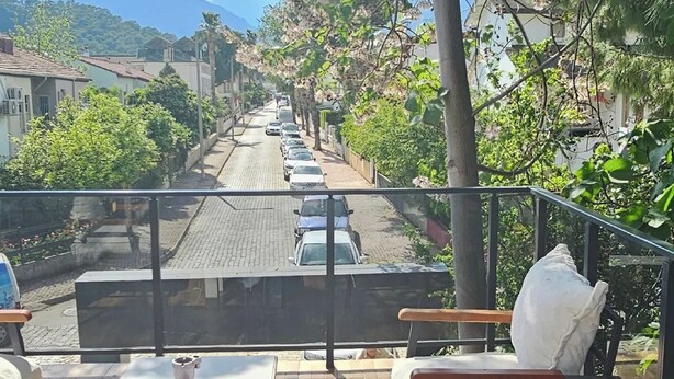 A balcony with outdoor seating, overlooking a street with parked cars and houses. - World Cities Residence (Kemer)
