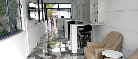 A modern interior with a marble floor, a seating area with a beige sofa and a small table, and a reception desk with chairs.