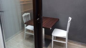 Una puerta de vidrio da a un patio con una mesa y dos sillas, una lámpara y una pared gris.