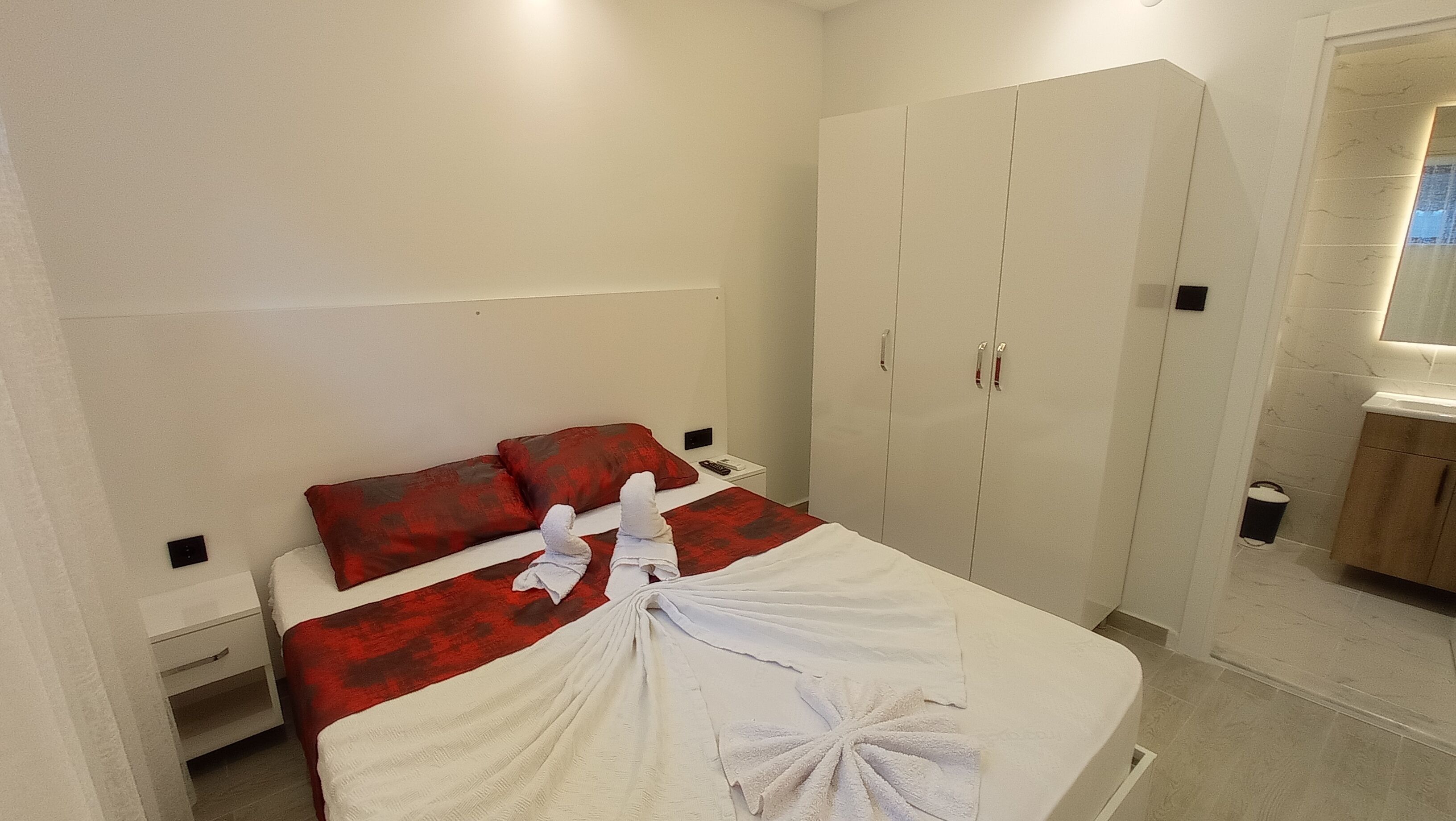 A bedroom with a bed, red and white bedding, a wardrobe, and a small bedside table.