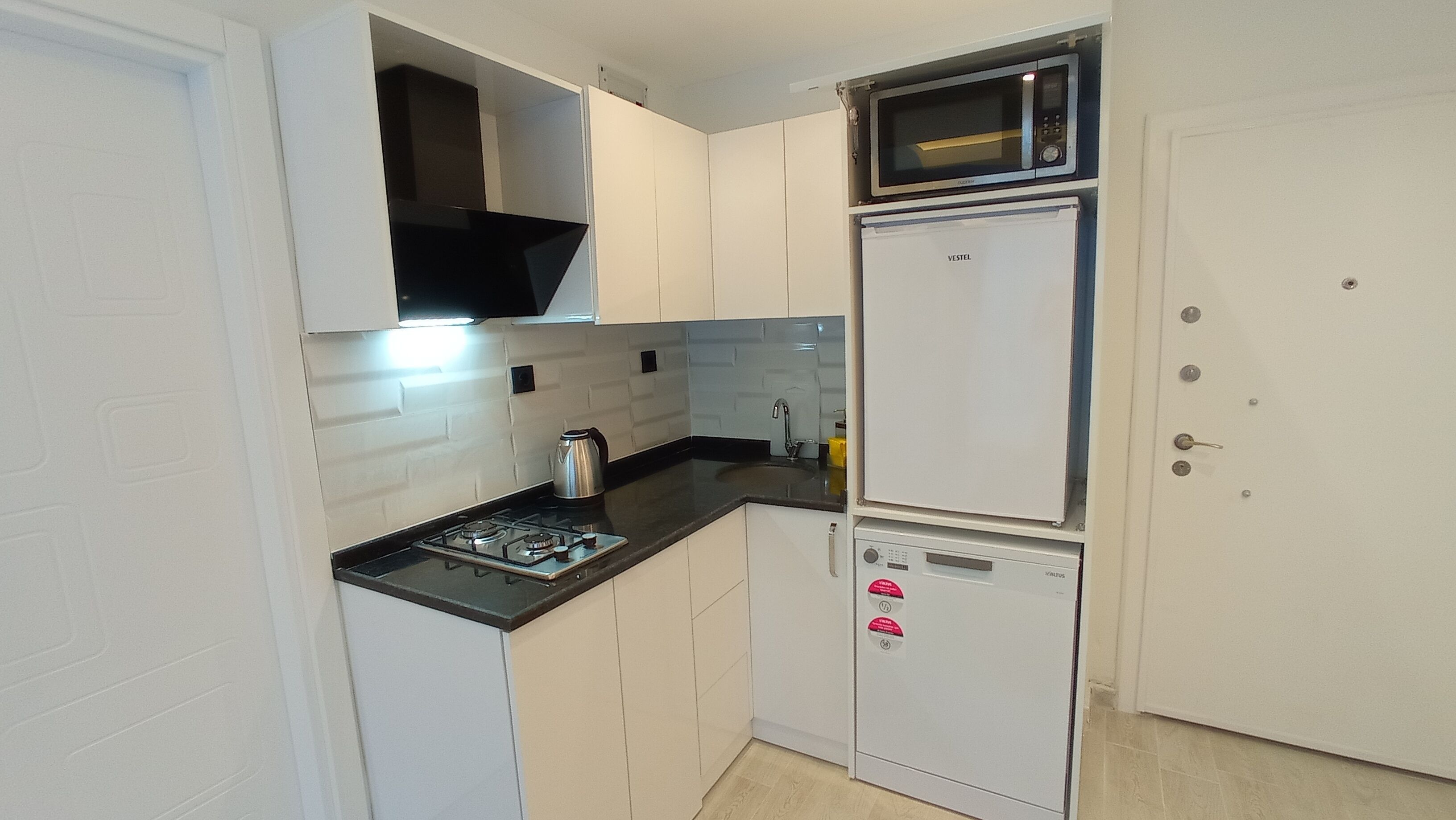 Una cocina compacta con armarios blancos, encimera negra, estufa, microondas y refrigerador.