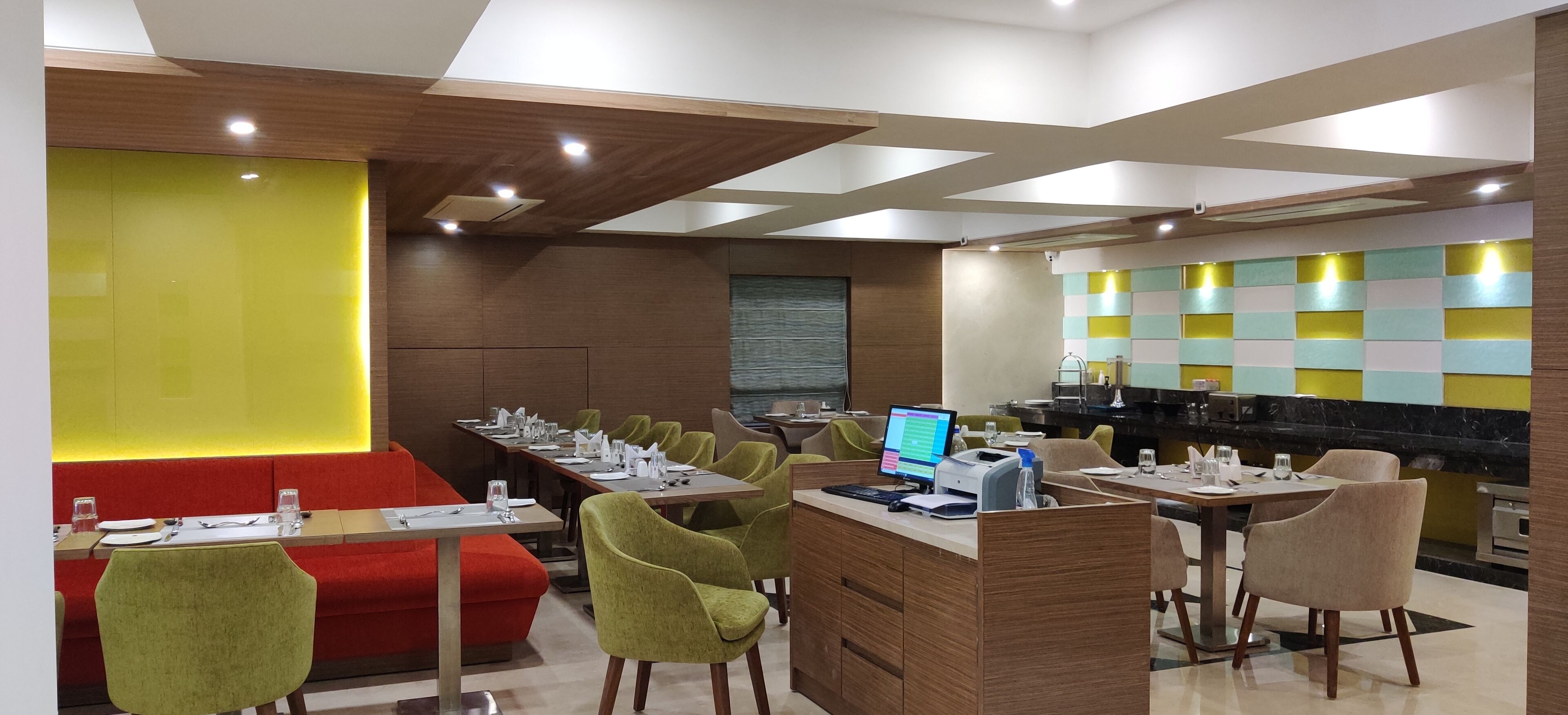 A modern dining area with multiple tables and chairs, a counter with a computer, and a vibrant wall design.