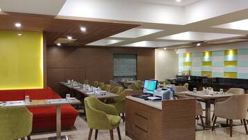 A modern dining area with multiple tables and chairs, a counter with a computer, and a vibrant wall design.
