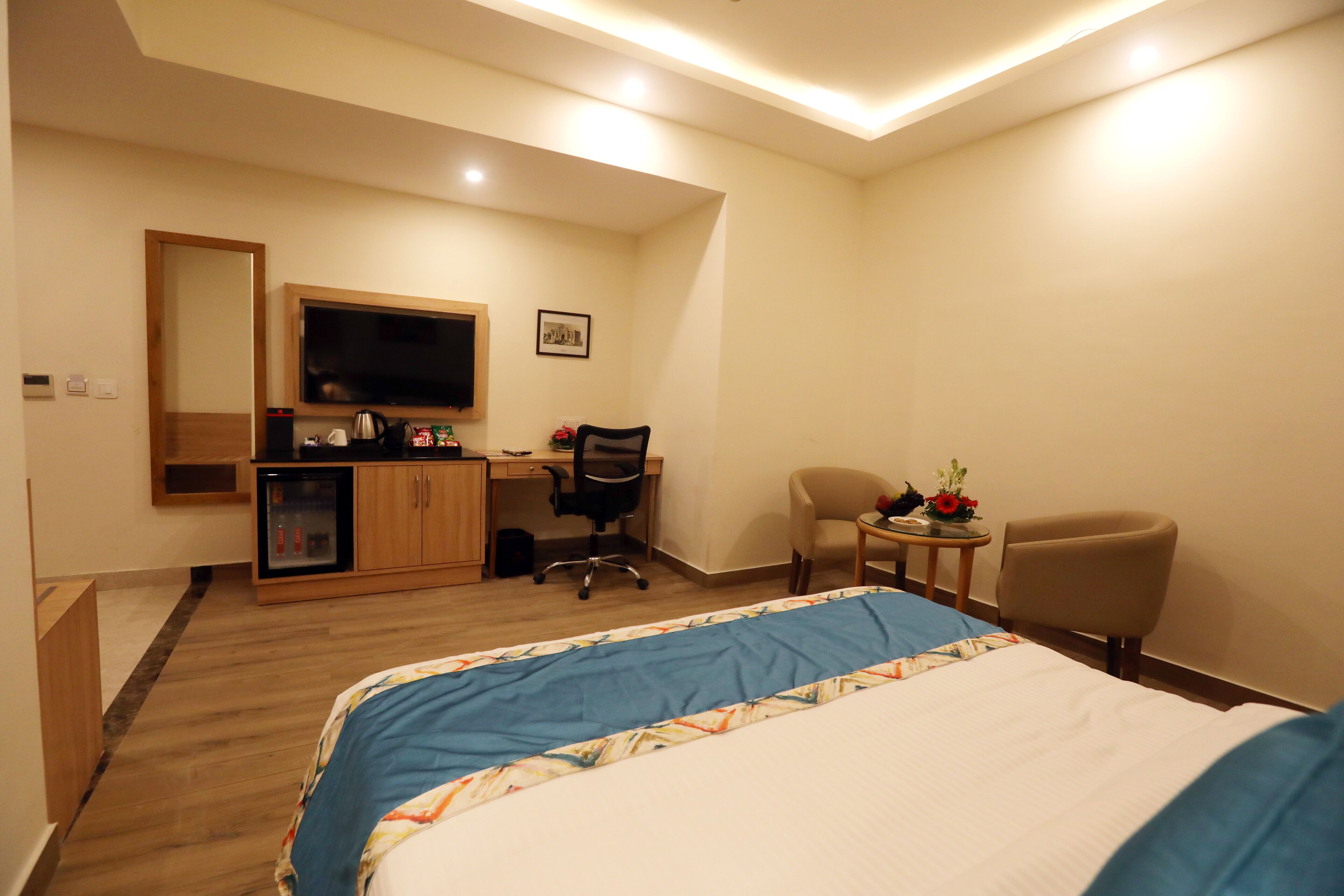 A hotel room with a bed, a desk, a chair, a television, and a small table with a flower vase.