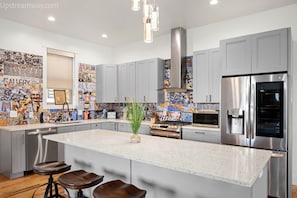 Une cuisine moderne avec des meubles gris, des appareils en acier inoxydable et un îlot central doté de tabourets de bar.