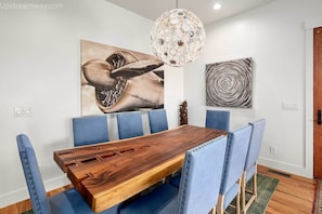 Un espace de repas moderne avec une table en bois, des chaises à revêtement bleu et des œuvres d’art abstraites accrochées au mur.