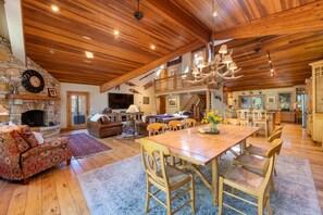 Un vaste espace de vie doté d’une cheminée en pierre, d’un plafond en bois et d’une table à manger avec des chaises.