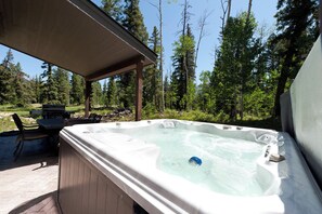 A hot tub in a forested area with a covered seating area and a grill.
